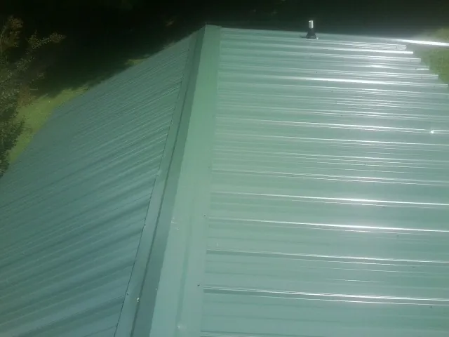 New green metal panels meeting at the ridge of a roof — Flat Roof Repair work by our crew in Roswell